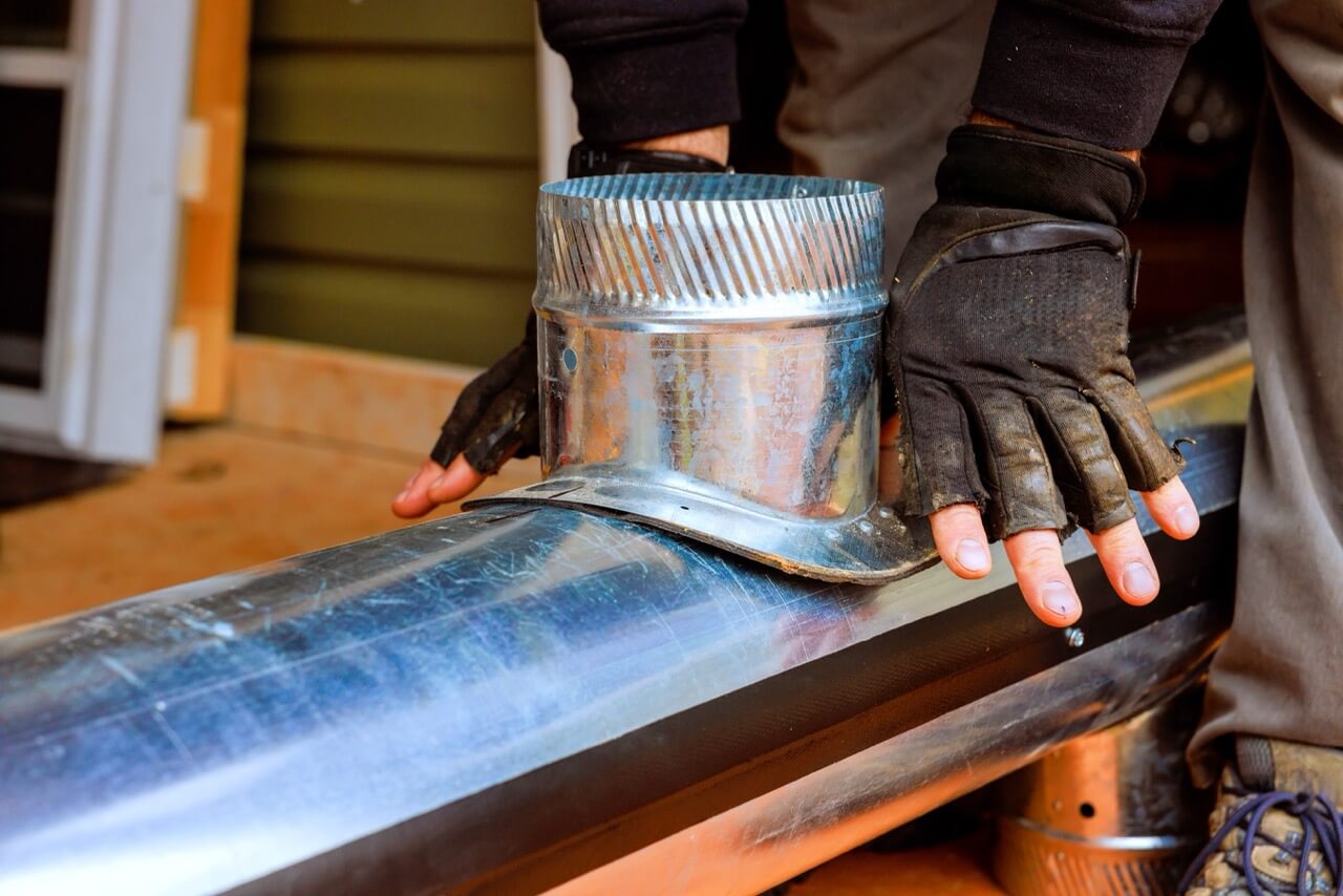 Man wearing safety gloves fitting metal duct for HVAC