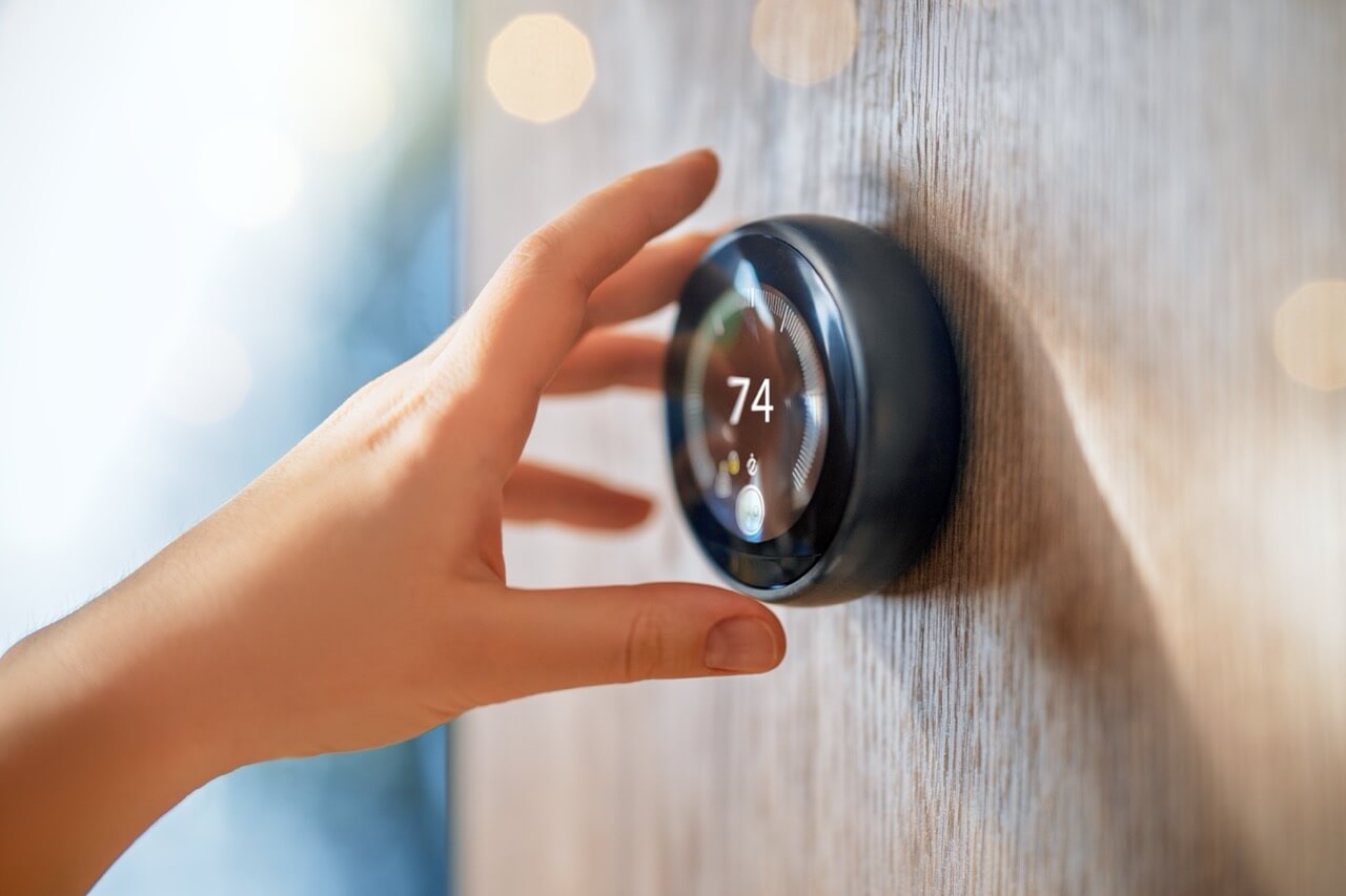 The hand reaching for the thermostat. Concept of smart home.
